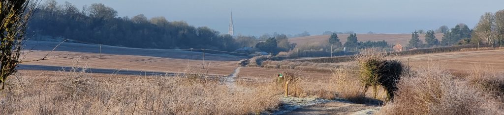 a frosty view of fields with a path winding through them towards Salisbury with the Cathederal visible in the distance