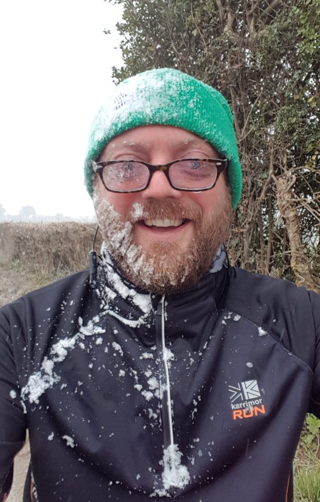 middle-aged man with beard, glasses and green hat, covered in snow after being caught in a snowstorm
